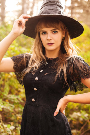 Young woman in black cape carrying spooky jack o lantern and looking away on Halloween day in autumn...