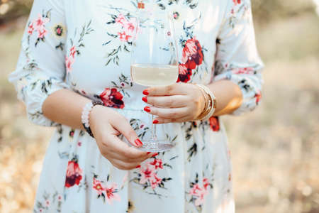 Unrecognizable female in floral dress enjoying white wine on sunny summer day in nature