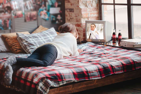 Unrecognizable female relaxing on comfortable bed with checkered blanket and watching retro TV at homeの写真素材