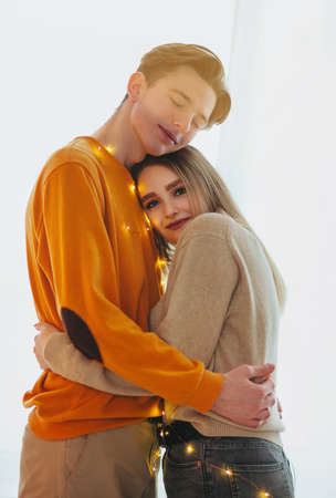 Side view of young man with closed eyes embracing girlfriend with fairy lights against white backgroundの写真素材