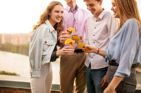 Happy men and women clinking glasses of fruit cocktails and proposing toast during the party