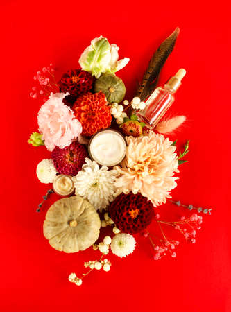 Set of natural cosmetic products, face cream and dropper bottle with essential oil on red background with colorful flowers, flat lay image. Skincare, beauty and natural cosmetics conceptの写真素材