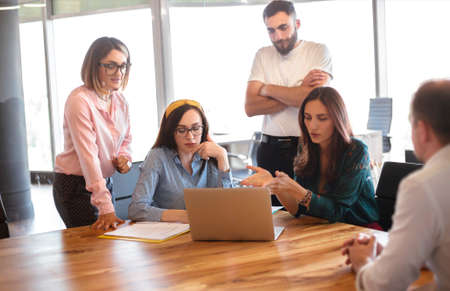 Woman in smart casual clothes sitting on chair and talking with workers during meeting in modern...