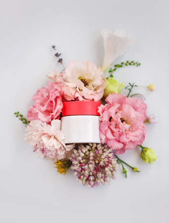 Top view of jar of face cream made from natural plant ingredients, oils and herbs, carnation and rose flowers on white blank background, vertical shot. Organic cosmetics conceptの写真素材