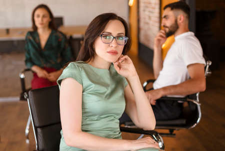 Woman in smart casual clothes sitting on chair with workers during meeting in modern workplaceの写真素材
