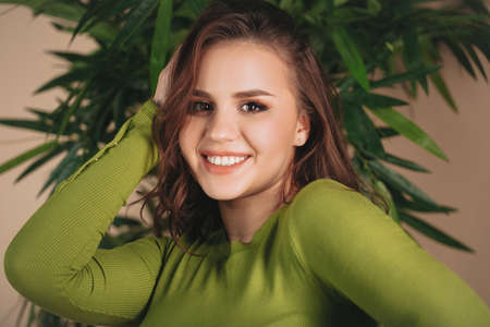 Closeup portrait of young happy brunette woman with serious facial expression standing sideways and looking straight at camera in bright green shirt isolated over beige background with copy spaceの写真素材