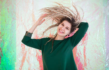 Cheerful young female in colorful outfit looking at camera with smile and shaking dreadlocks...