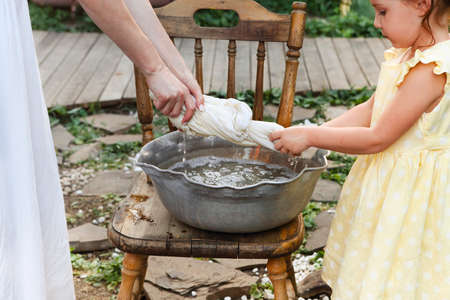Mom and little daughter spending time and doing household chores together outside in village,...