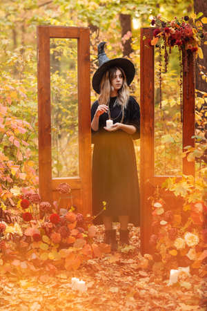 Young woman in Witch costume and hat looking mysteriously at candle in her hands isolated against...