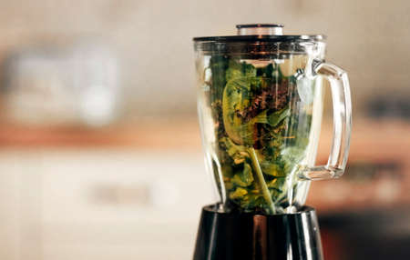 Close up photo of green vegetable smoothie blender machine in kitchen with kale leaves inside ready...