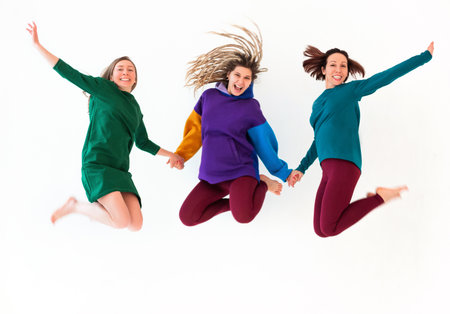 Image of three happy playful barefoot women of different age holding hands together, jumping and...