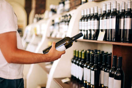 Anonymous male customer examining bottle while standing near shelves and selecting wine in storeの写真素材