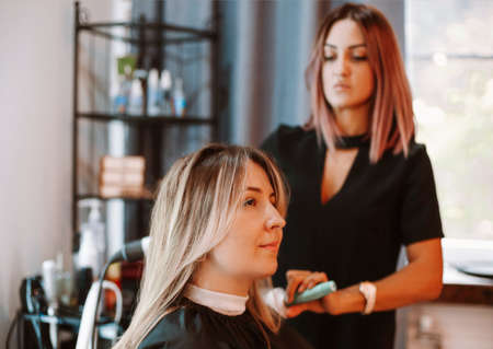 Happy woman with stylist making hairdo at salon. Competent female hairdresser deciding what to do in hair salon with brunette female client. Two beautiful ladies discussing new hairstyle. Professional coiffure and stylist work conceptの写真素材