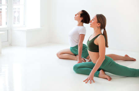 Two young women doing yoga indoor, sitting in position isolated over white studio background. Sport, yoga and healthy lifestyle conceptの写真素材