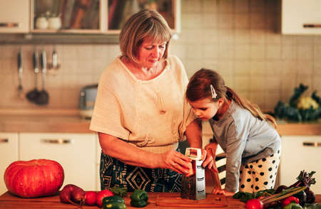 Family portrait of grandmother and granddaughter cooking together in kitchen at home, granny showing...