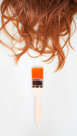 Cropped shot of female red hair curls and wide paint brush with wooden handle on white background with copy space for text, flat lay image. Beauty salon service conceptの写真素材