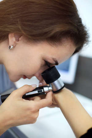 Close-up photo of young brunette woman dermatologist examines nevus or birthmarks on patients hand with dermatoscope. Prevention of melanoma, mole control. Professional dermoscopy conceptの写真素材