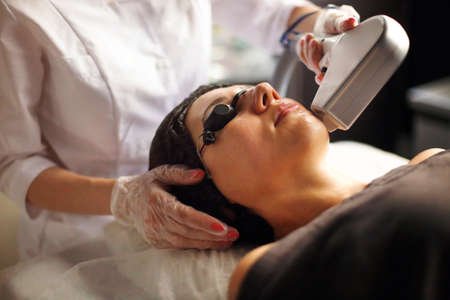 From above of female client lying on couch in beauty salon during laser epilation of her face