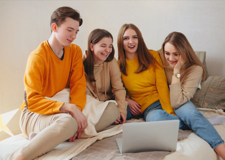 Happy teenage friends watching funny content on laptop and laughing