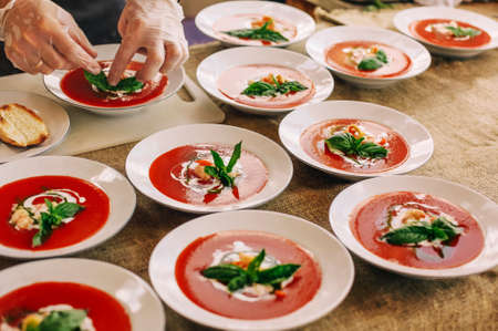 Many bowls of various gazpacho soups with ingredients cooking by chef