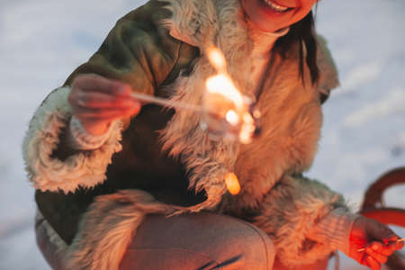Cropped shot of happy woman roasting frying sweet marshmallow over the camp fire in winter forest,...