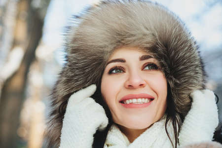Funny young woman in furry hood looking away on blurred background of street on winter dayの写真素材