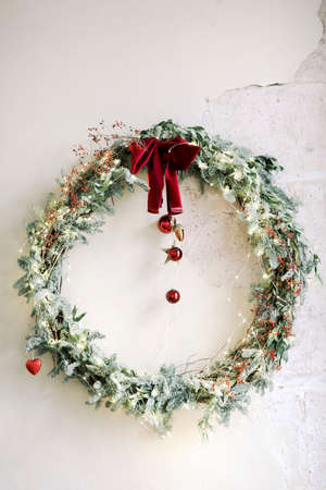 Stylish Christmas wreath with red bow and baubles hanging on shabby concrete wall during holiday celebrationの写真素材