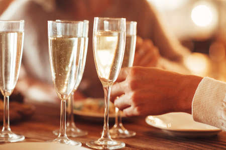 Unrecognizable female taking wineglass with champagne while standing near banquet table with burning candles during Christmas party at homeの写真素材