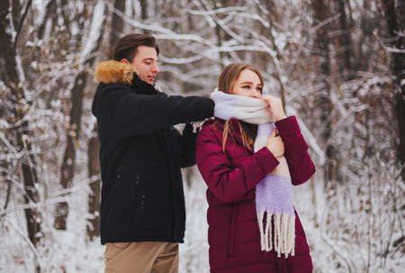 Photo of beautiful young teen couple spending time together outside in cold winter, guy straightening knitted girls scarf to keep her warm on frosty day. Romantic date outdoorsの写真素材