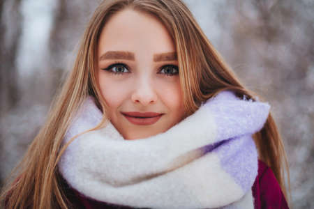 Closeup photo of beautiful female with sharp look, half of young woman face covered with light colored knitted scarf, girl looking into camera with dark brown eyes with black eyeliner makeupの写真素材
