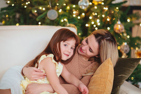 Happy playful little girl daughter playing with positive mother, spending time together during Christmas holidays at home, mom and child having fun in living room with New Year treeの写真素材