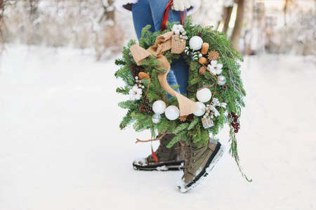 Unrecognizable female in outerwear carrying decorated Christmas wreath and standing on snow on sunny winter dayの写真素材