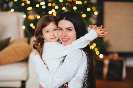 Happy playful little girl daughter playing with positive mother, spending time together during Christmas holidays at home, mom and child having fun in living room with New Year treeの写真素材
