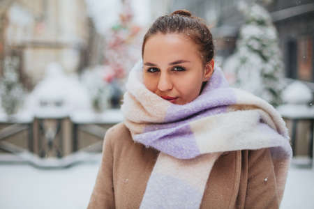 Closeup photo of beautiful brunette female with sharp look, half of young woman face covered with light colored knitted scarf, girl looking into camera with dark brown eyes with black eyeliner makeupの写真素材