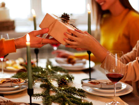 Happy person giving wrapped gift to friend while sitting at table and celebrating Christmas togetherの写真素材