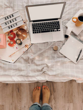 Top view of cozy blogger workplace with mockup laptop, agenda, coffee cup and decorations on bed at home in morning, flat lay photo. Freelance work conceptの写真素材
