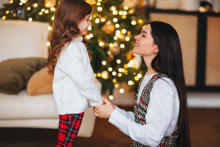 Happy playful little girl daughter playing with positive mother, spending time together during Christmas holidays at home, mom and child having fun in living room with New Year treeの写真素材