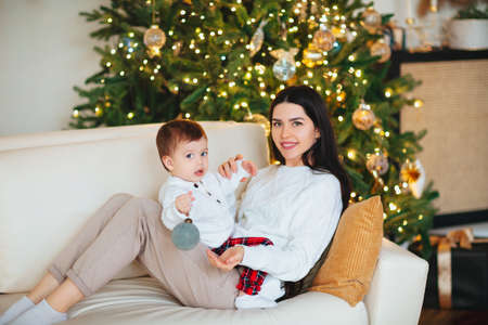 Young woman smiling and playing with cute boy on blurred background of decorated coniferous tree on...