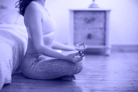 Smiling young brown haired woman in pajamas practicing yoga in bright bedroom in the morning. Color of 2022 year, very peri, tonedの写真素材