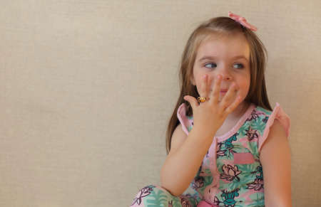 Close up of cute adorable smiling little girl with blue eyes against beige wall indoors, happy kid...