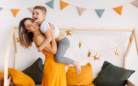 Young happy family loving mother and her child son having fun together at home, playing and laughing. Smiling kid hugging embracing his mom, happy to spend leisure time on weekend with mommyの写真素材