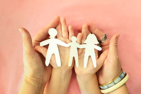 Cropped shot of mother, father and child holding family paper cut out in hands, isolated on pink background. cardboard figures of parents and kid holding hands together. International Day of Familiesの写真素材