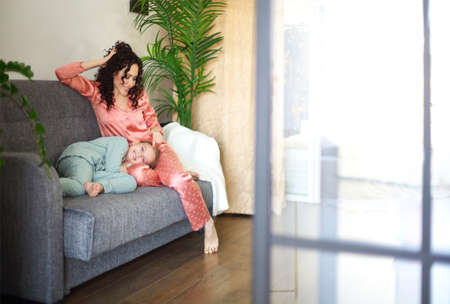 Cozy domestic photo of happy mother and daughter in pajamas relaxing on sofa in the morning, young beautiful mom and little girl child spending lazy family weekend at home. family and motherhood conceptの写真素材