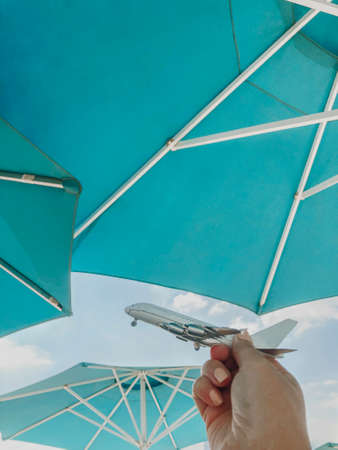 Creative photo shot of female hand holding aircraft plane miniature against backdrop of open beach...