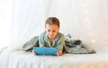 Children and modern technologies. Little girl lying in pajama with modern digital tablet on canopy...