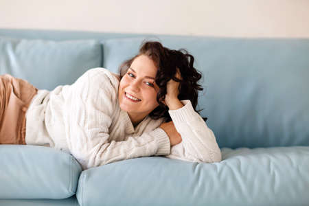 Close up of young Caucasian woman lying down on blue sofa indoor, fell asleep in casual outwear...