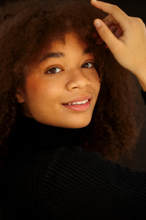 Portrait of attractive smiling curly african-american woman in black clothes looking at camera,...