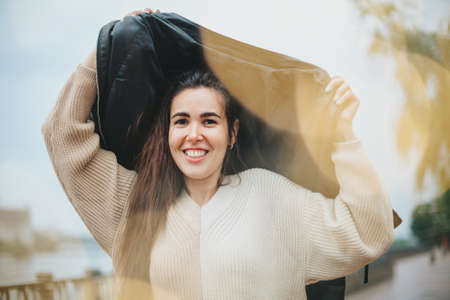 Young happy cheerful woman under rain in storm on autumn day standing on city street, positive...