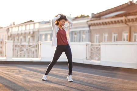 Full-length of young carefree african american woman jumping at rooftop in morning sunlight with...