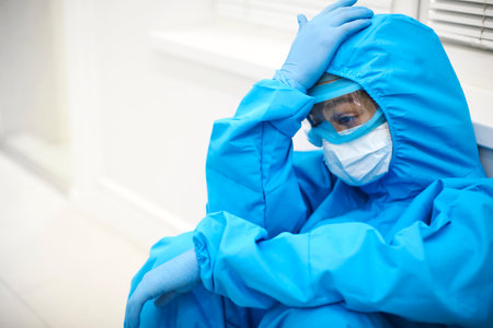 Tired female doctor in personal protective equipment PPE feeling depressed after difficult stressful...